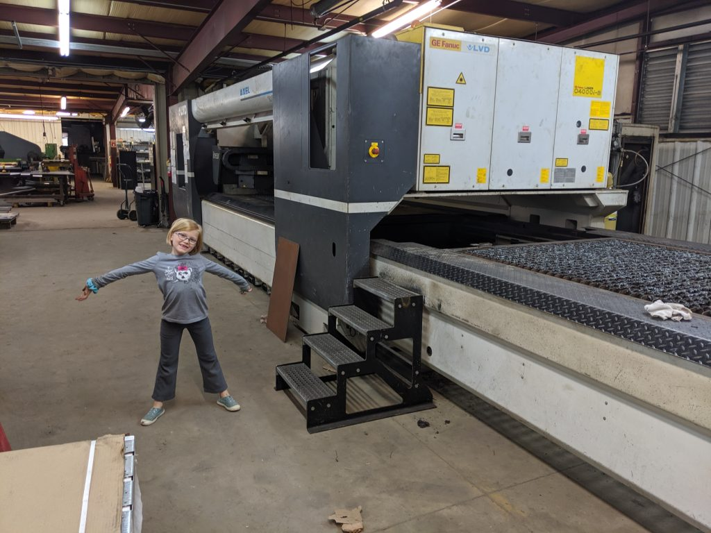 Claire stands in front of a new laser cutting machine ready to make parts