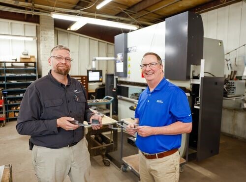 two men stand in front of a new machine smiling