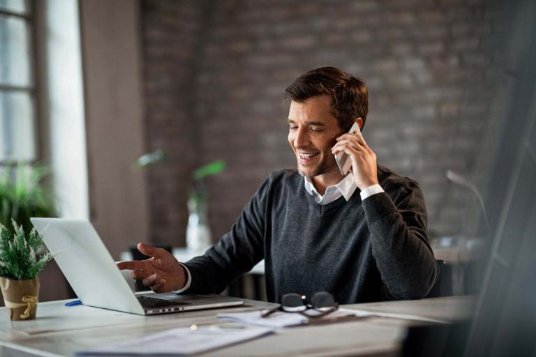 stock image of a man answering a telephone while looking at a computer.